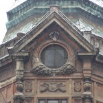 Przyczółek na ściętej fasadzie, a pod nim okrągłe okno ozdobione rogami obfitości oraz litery M L O - inicjały pierwszego właściciela